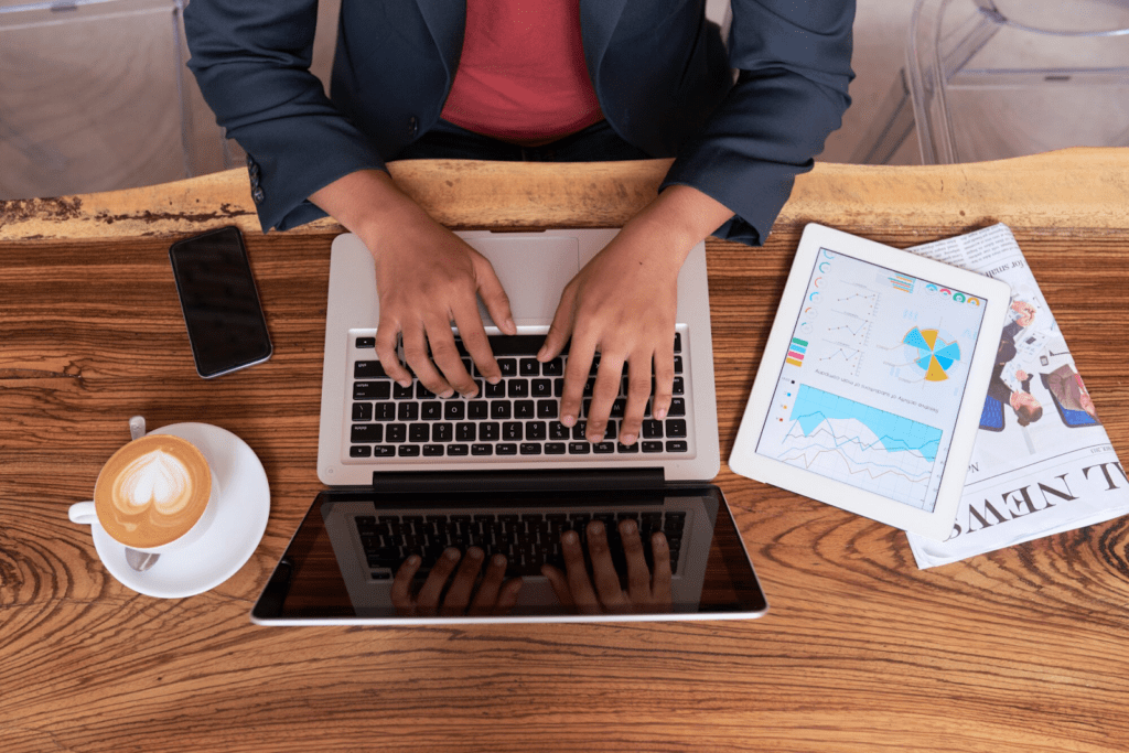 Hands of a man sitting at a wooden table in a cafe and working on a laptop